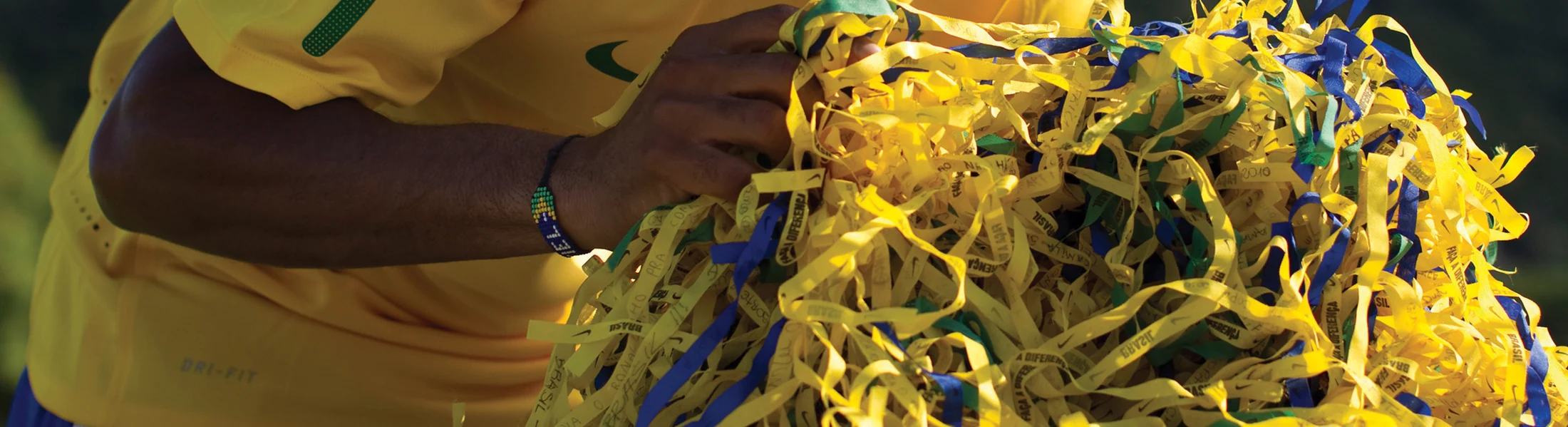 Braços e mãos de um jogador da seleção seguram um grande conjunto de fitas da torcida.
