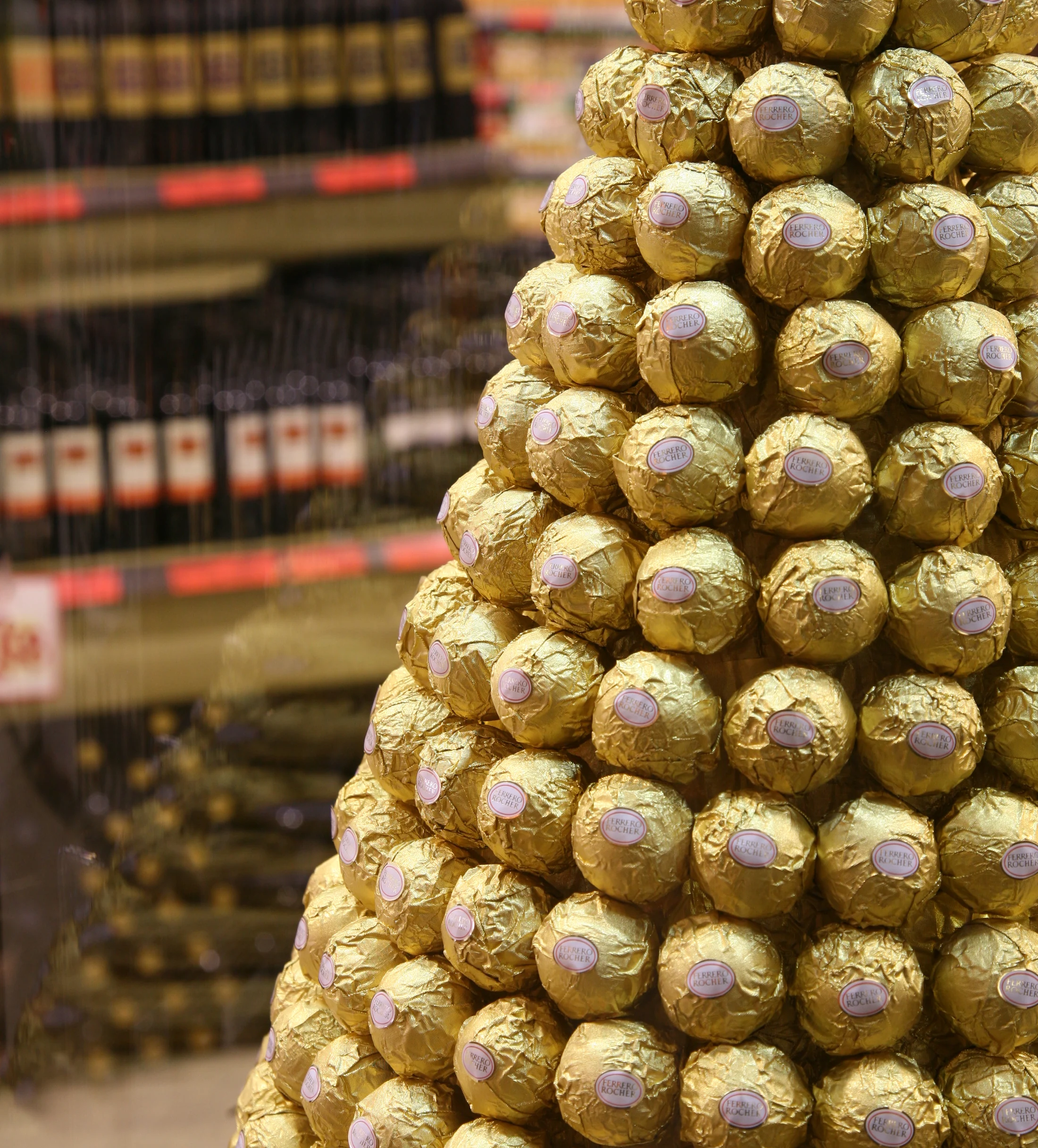 Detalhe da torre de chocolates Ferrero Rocher diante das prateleiras do supermercado.