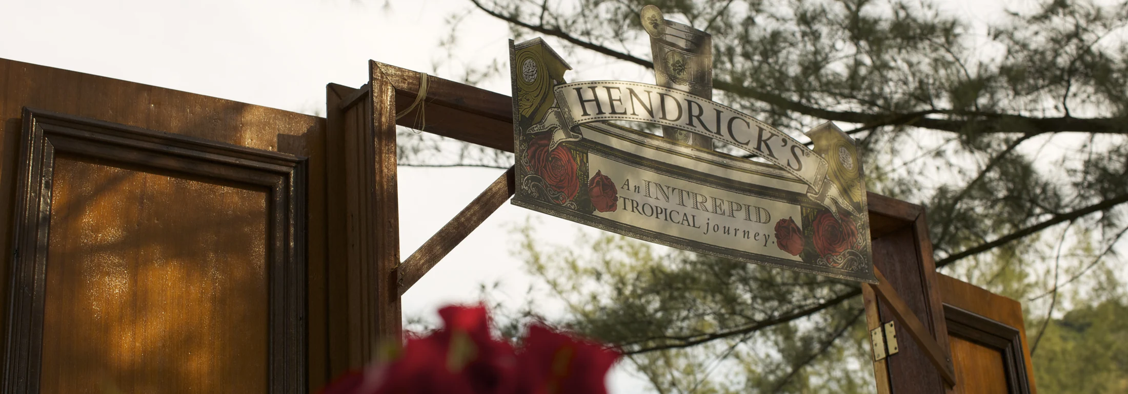 Portal de madeira com a placa Hendrick’s An Intrepid Tropical Journey em ambiente externo.
